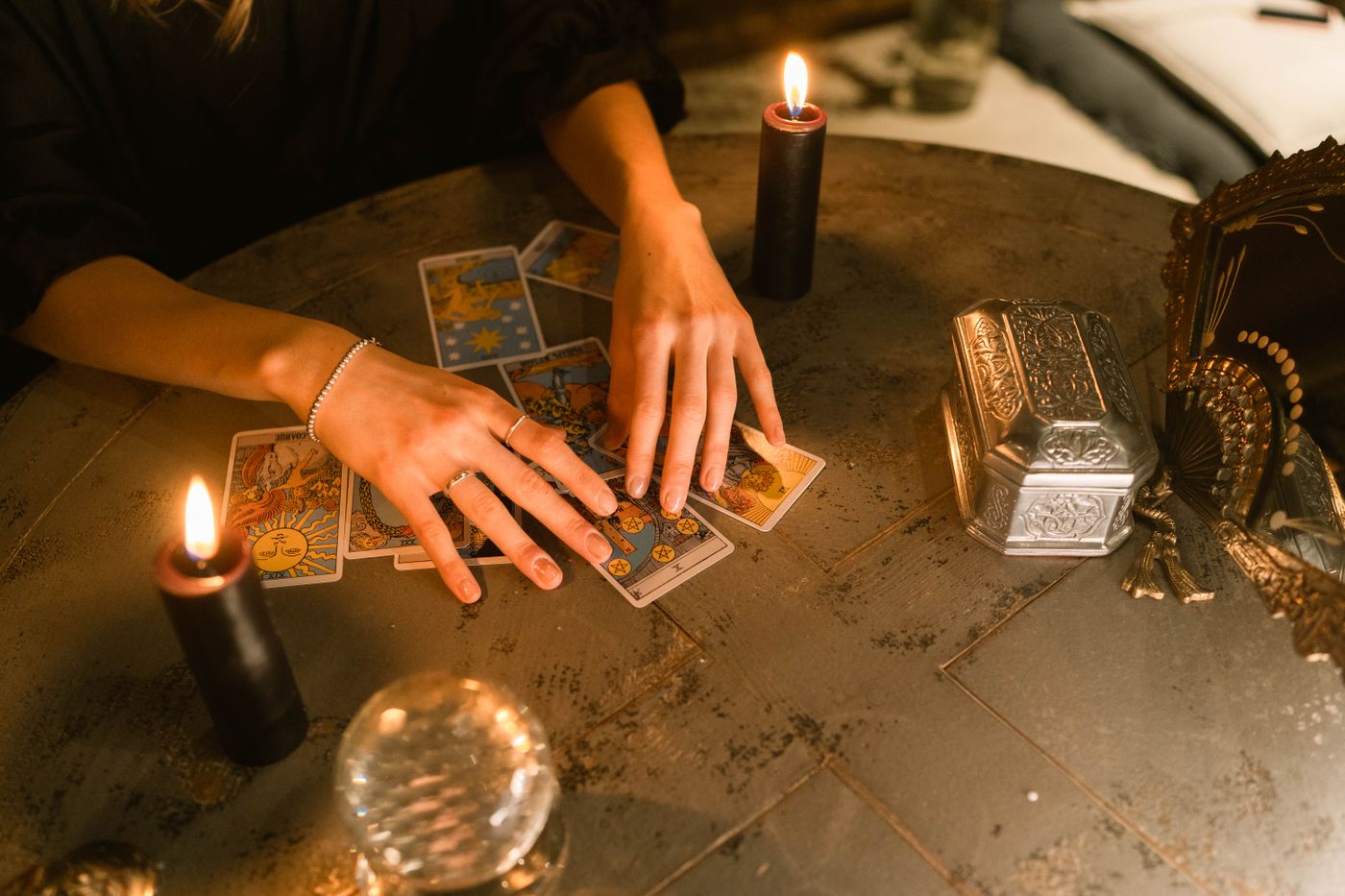 Hands arranging physical tarot cards beside warm candlelight